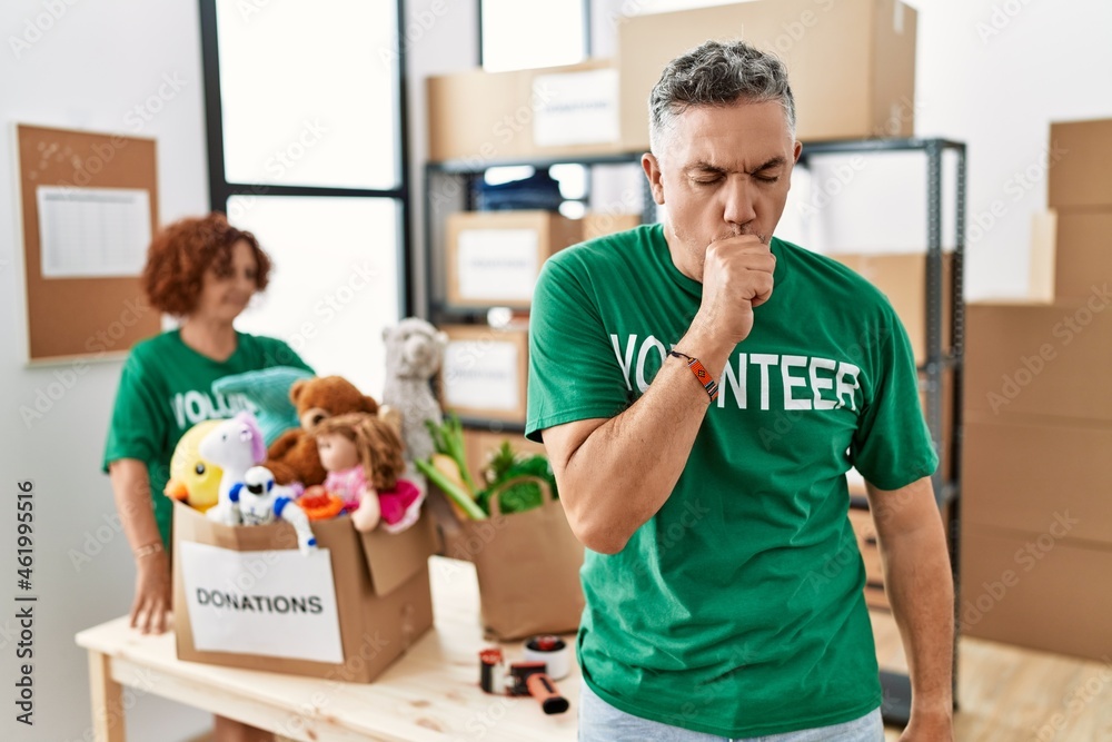 Middle age man wearing volunteer t shirt at donations stand feeling unwell and coughing as symptom for cold or bronchitis. health care concept. Middle age man wearing volunteer t shirt at donations stand feeling unwell and coughing as symptom for cold or bronchitis. health care concept.