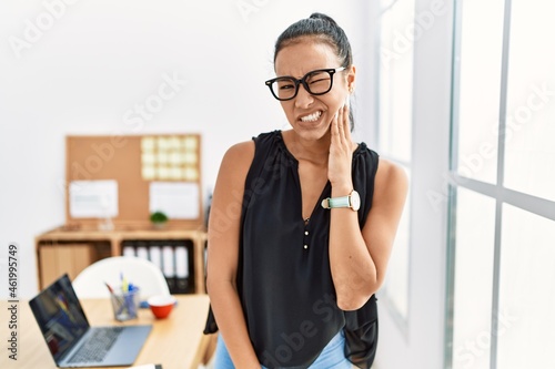 Young hispanic business woman working at the office touching mouth with hand with painful expression because of toothache or dental illness on teeth. dentist