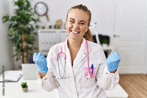 Young caucasian woman wearing doctor uniform and stethoscope at the clinic very happy and excited doing winner gesture with arms raised  smiling and screaming for success. celebration concept.
