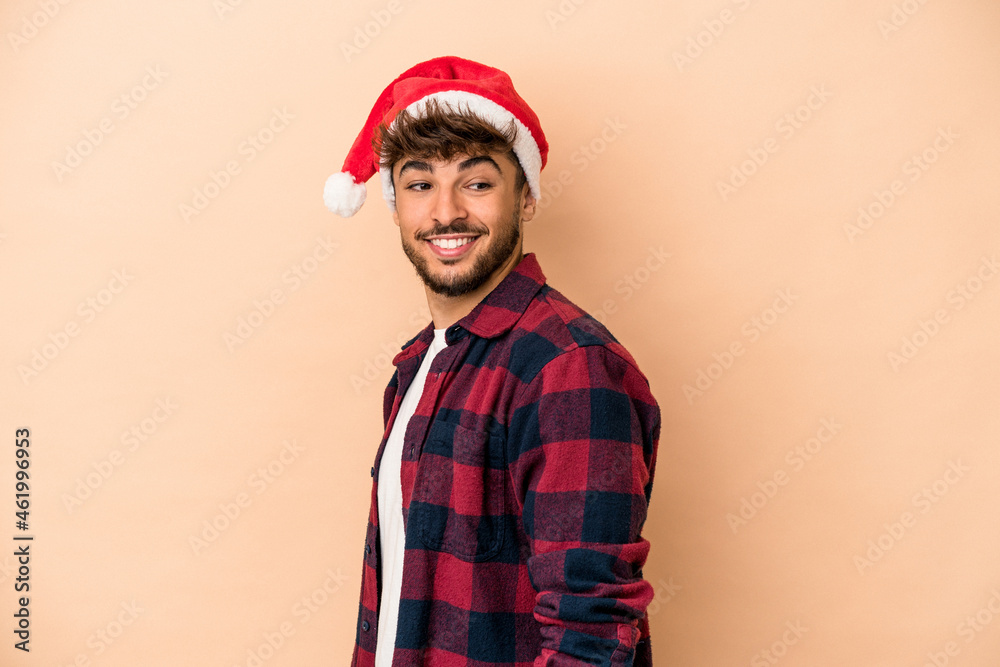Young arab man celebrating Christmas isolated on beige background looks aside smiling, cheerful and pleasant. Young arab man celebrating Christmas isolated on beige background looks aside smiling, cheerful and pleasant.