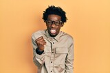 Young african american man wearing casual clothes and glasses angry and mad raising fist frustrated and furious while shouting with anger. rage and aggressive concept.