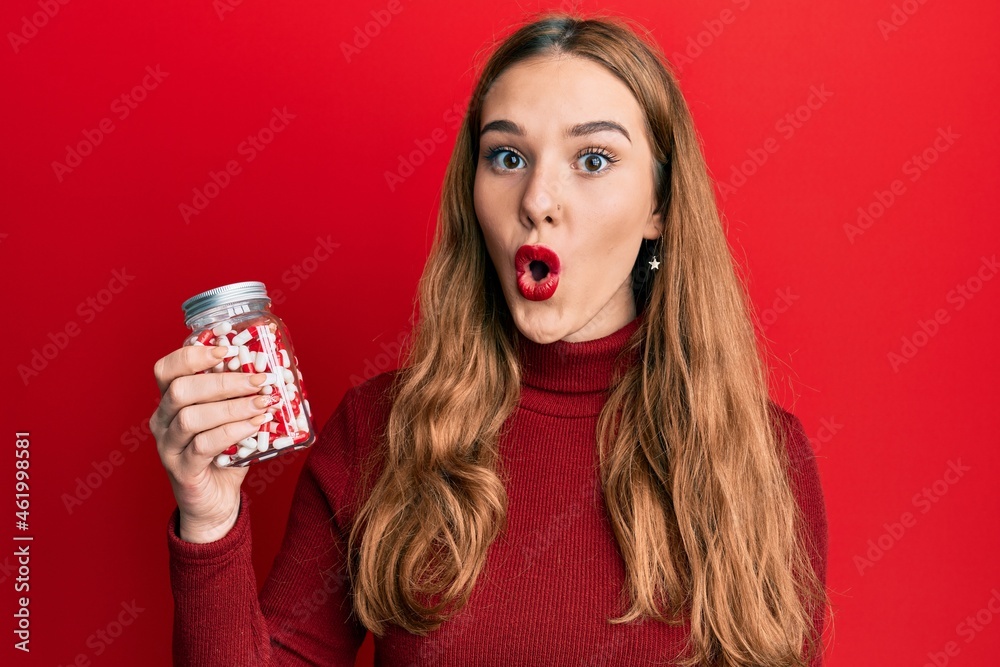 Young blonde woman holding jar of pills scared and amazed with open mouth for surprise, disbelief face Young blonde woman holding jar of pills scared and amazed with open mouth for surprise, disbelief face