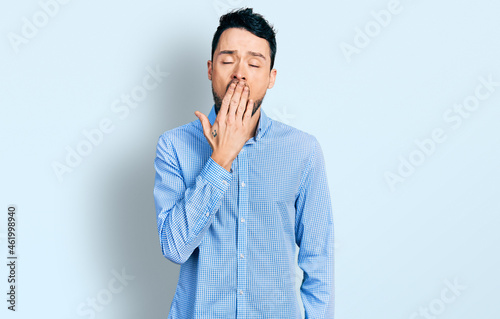 Hispanic man with beard wearing casual business shirt bored yawning tired covering mouth with hand. restless and sleepiness.