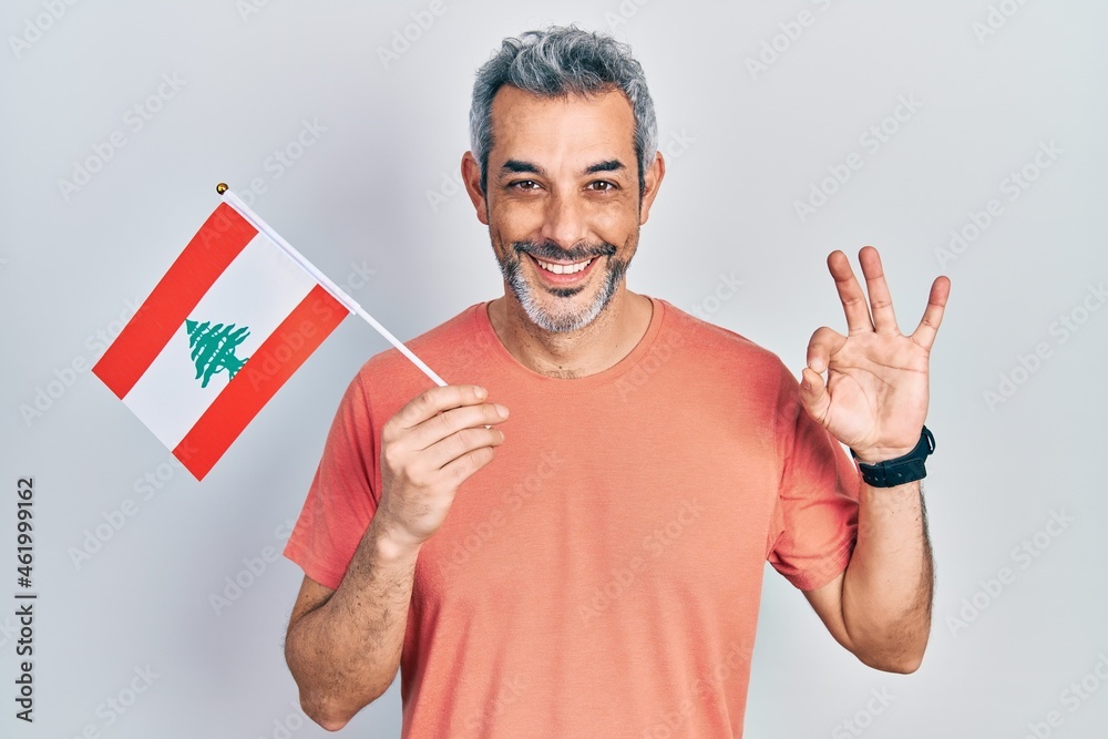 Handsome middle age man with grey hair holding lebanon flag doing ok sign with fingers, smiling friendly gesturing excellent symbol Handsome middle age man with grey hair holding lebanon flag doing ok sign with fingers, smiling friendly gesturing excellent symbol