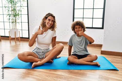 Young woman and son sitting on training mat at the gym smiling happy and positive, thumb up doing excellent and approval sign
