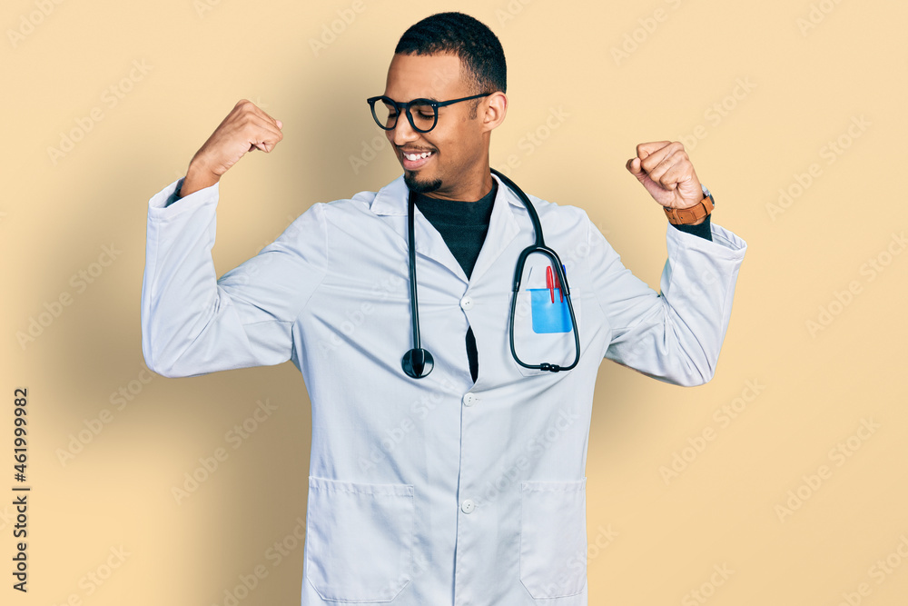 Young african american man wearing doctor uniform and stethoscope showing arms muscles smiling proud. fitness concept. Young african american man wearing doctor uniform and stethoscope showing arms muscles smiling proud. fitness concept.