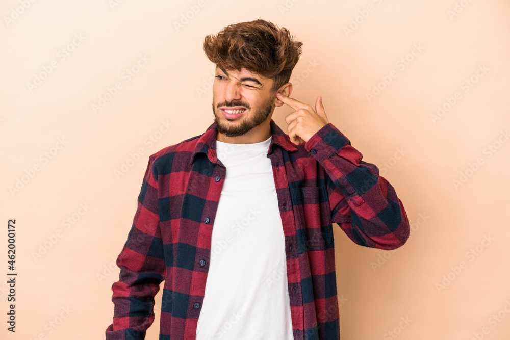 Young arab man isolated on beige background covering ears with hands. Young arab man isolated on beige background covering ears with hands.