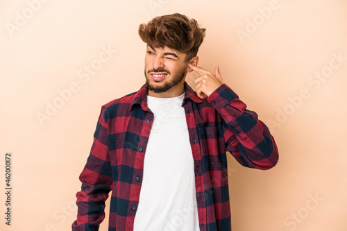 Young arab man isolated on beige background covering ears with hands.