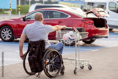 Person with a physical disability pushes a cart towards a car in a supermarket parking lot © romaset