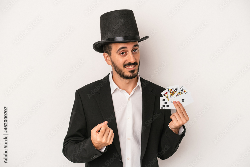 Young magician man holding a magic card isolated on white background pointing with finger at you as if inviting come closer. Young magician man holding a magic card isolated on white background pointing with finger at you as if inviting come closer.