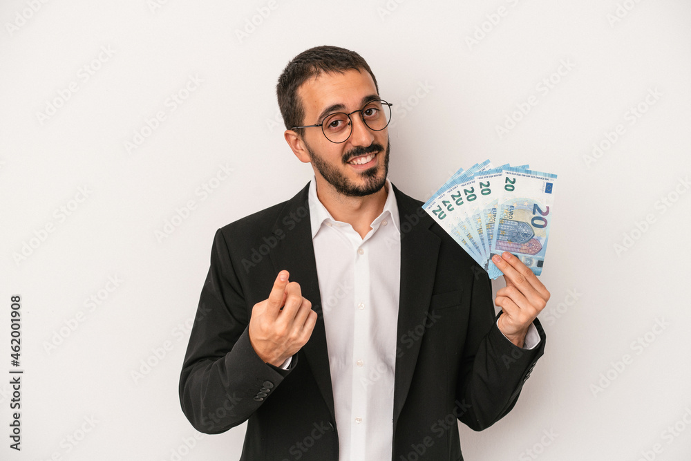 Young caucasian business man holding banknotes isolated on white background pointing with finger at you as if inviting come closer. Young caucasian business man holding banknotes isolated on white background pointing with finger at you as if inviting come closer.