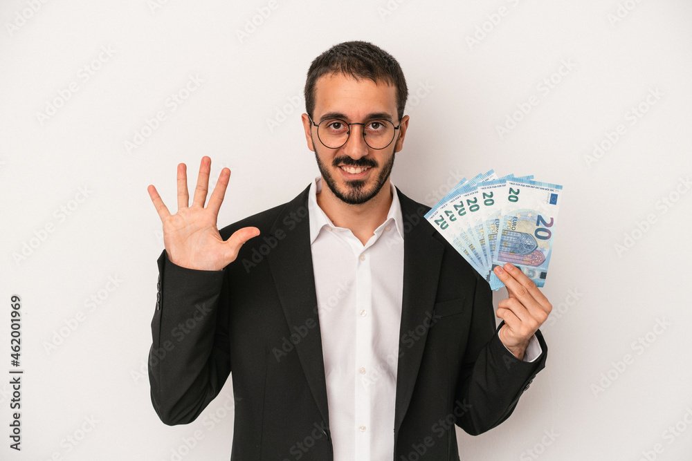 Young caucasian business man holding banknotes isolated on white background smiling cheerful showing number five with fingers. Young caucasian business man holding banknotes isolated on white background smiling cheerful showing number five with fingers.