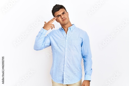 Young hispanic man wearing business shirt standing over isolated background shooting and killing oneself pointing hand and fingers to head like gun, suicide gesture.
