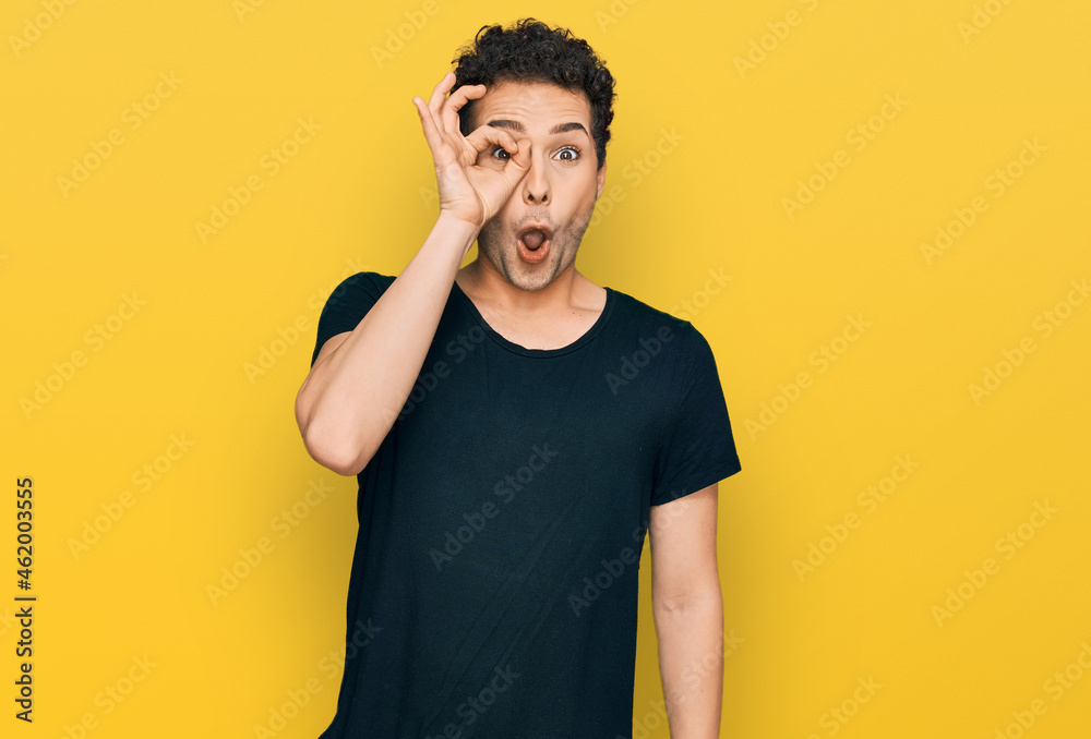 Young handsome man wearing casual black t shirt doing ok gesture shocked with surprised face, eye looking through fingers. unbelieving expression. Young handsome man wearing casual black t shirt doing ok gesture shocked with surprised face, eye looking through fingers. unbelieving expression.