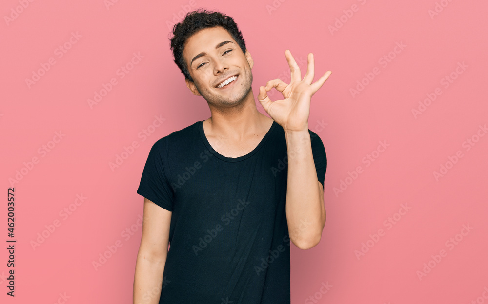 Young handsome man wearing casual black t shirt smiling positive doing ok sign with hand and fingers. successful expression.