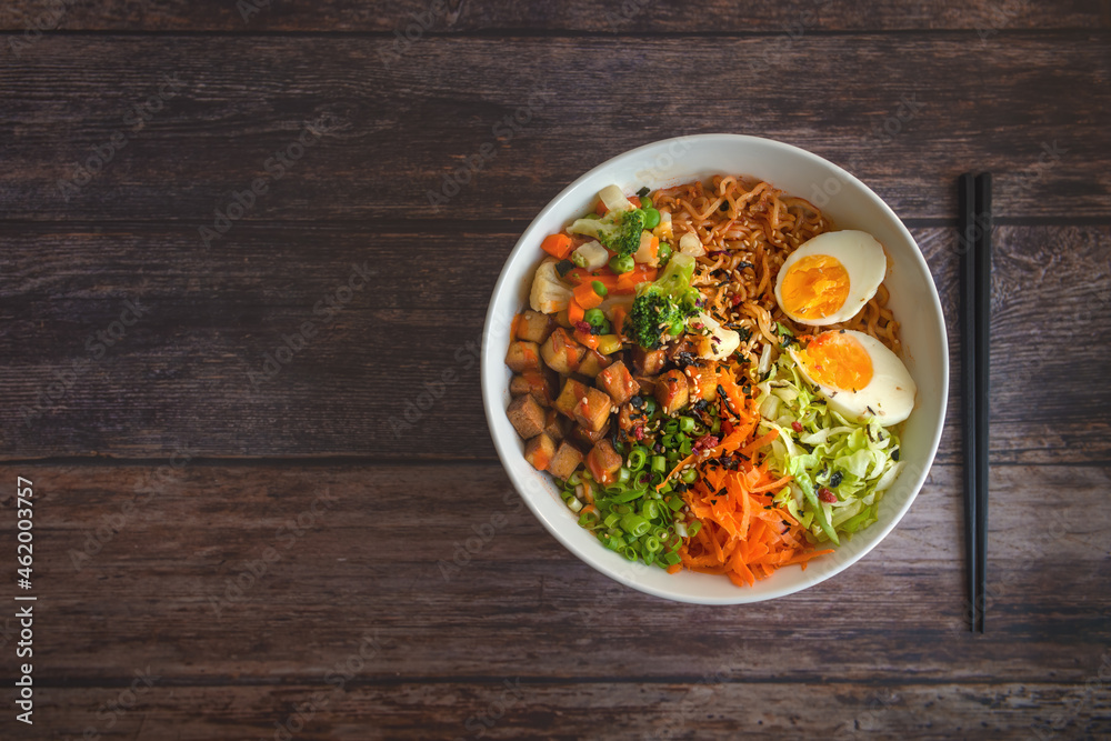 Variation of ramen homemade soup with noodles, marinated tofu, chopped carrots, onions, lettuce and broccoli in a bowl lying on a wooden table. Variation of ramen homemade soup with noodles, marinated tofu, chopped carrots, onions, lettuce and broccoli in a bowl lying on a wooden table.