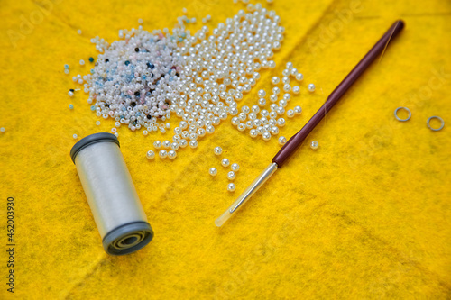 home handicrafts - beadwork - accessories for working with beads - white beads, hook, fishing line on a bright yellow background photo