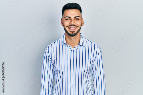 Young hispanic man with beard wearing casual striped shirt with a happy and cool smile on face. lucky person.