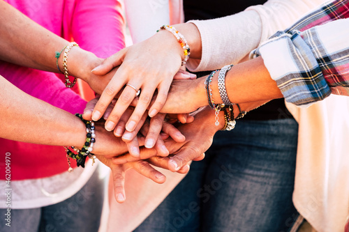 Close up of young people putting their hands together. Friends with stack of hands showing unity and teamwork. Close up of hands of women with accessories on wreist and fringers. photo