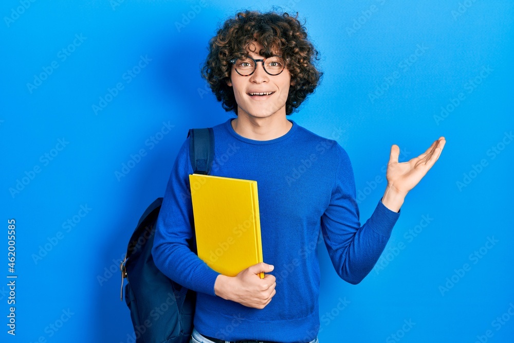 Handsome young man wearing student backpack and holding book celebrating victory with happy smile and winner expression with raised hands Handsome young man wearing student backpack and holding book celebrating victory with happy smile and winner expression with raised hands