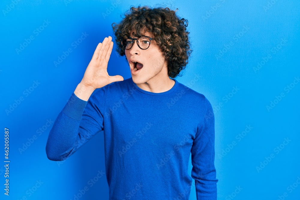 Handsome young man wearing casual clothes and glasses shouting and screaming loud to side with hand on mouth. communication concept.