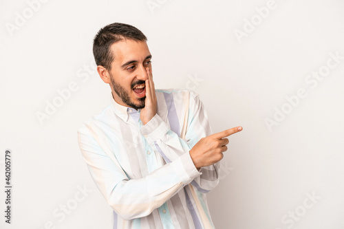 Young caucasian man isolated on white background saying a gossip, pointing to side reporting something.