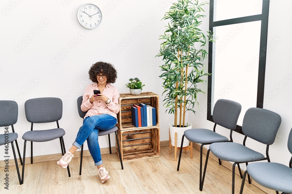 Fototapeta premium Young middle east woman using smartphone sitting on chair at waiting room