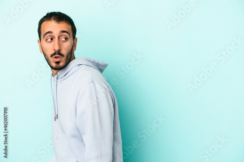 Young caucasian man isolated on blue background looks aside smiling, cheerful and pleasant.