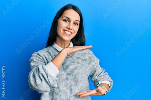 Young hispanic woman wearing casual clothes gesturing with hands showing big and large size sign, measure symbol. smiling looking at the camera. measuring concept.