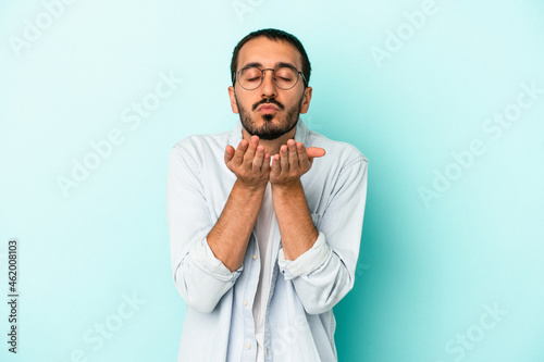 Young caucasian man isolated on blue background folding lips and holding palms to send air kiss.