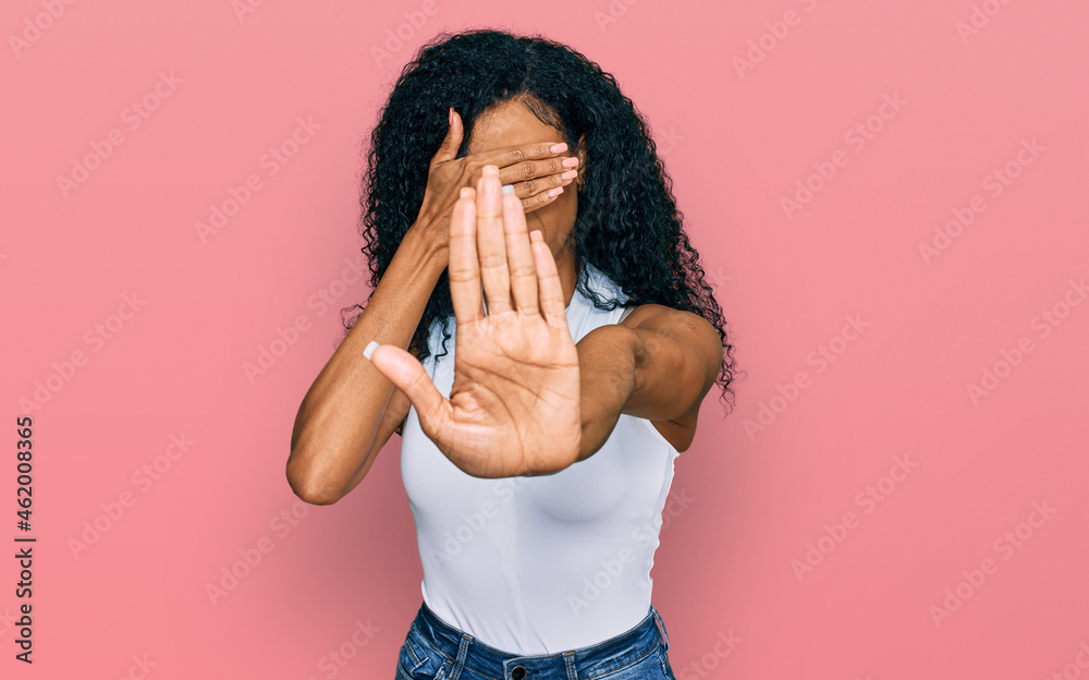 Middle age african american woman wearing casual style with sleeveless shirt covering eyes with hands and doing stop gesture with sad and fear expression. embarrassed and negative concept. Middle age african american woman wearing casual style with sleeveless shirt covering eyes with hands and doing stop gesture with sad and fear expression. embarrassed and negative concept.