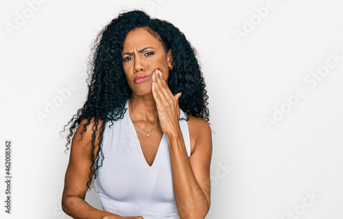 Middle age african american woman wearing casual style with sleeveless shirt touching mouth with hand with painful expression because of toothache or dental illness on teeth. dentist