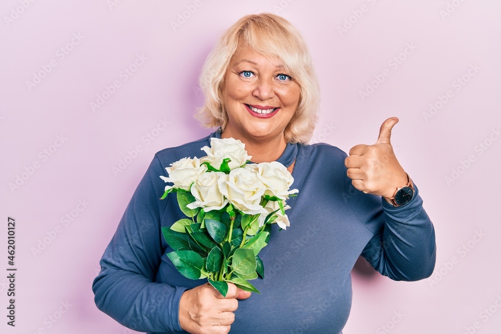 Middle age blonde woman holding flowers smiling happy and positive, thumb up doing excellent and approval sign Middle age blonde woman holding flowers smiling happy and positive, thumb up doing excellent and approval sign