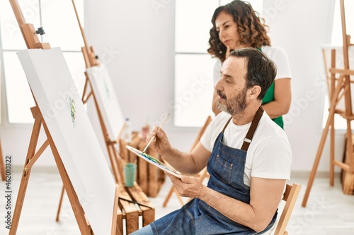 Middle age student and teacher with serious expression painting at art school.