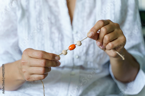 Close up on midsection of unknown female holding string with wooden or plastic pearls making nature materials bracelet necklace at home - Creative designer working Creativity hobby and leisure concept