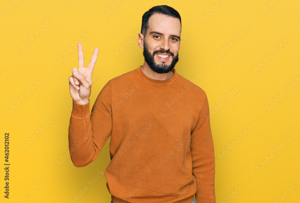 Young man with beard wearing casual winter sweater smiling with happy face winking at the camera doing victory sign. number two. Young man with beard wearing casual winter sweater smiling with happy face winking at the camera doing victory sign. number two.
