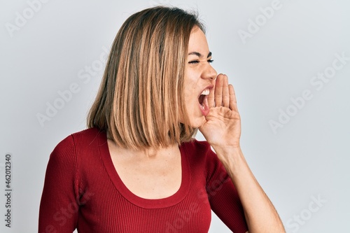 Young caucasian blonde woman wearing casual jumper shouting and screaming loud to side with hand on mouth. communication concept.