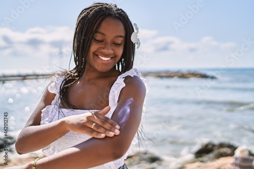 Young african american girl smiling happy using sunscreen lotion at the beach.