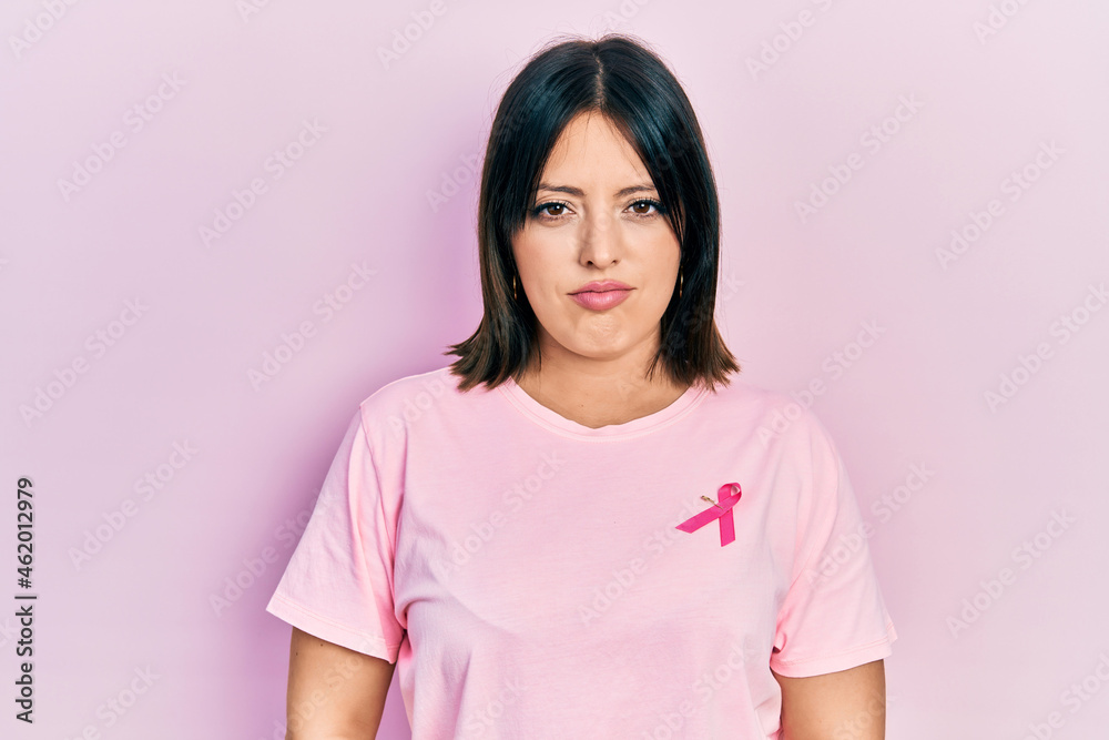 Fototapeta premium Young hispanic woman wearing pink cancer ribbon on t shirt skeptic and nervous, frowning upset because of problem. negative person.