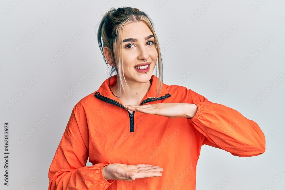 Young modern girl wearing sports sweatshirt gesturing with hands showing big and large size sign, measure symbol. smiling looking at the camera. measuring concept. Young modern girl wearing sports sweatshirt gesturing with hands showing big and large size sign, measure symbol. smiling looking at the camera. measuring concept.