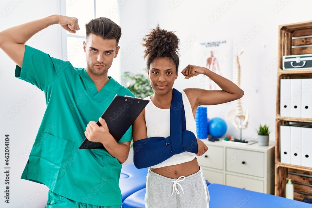 Physiotherapist working with patient wearing arm on sling at rehabilitation clinic strong person showing arm muscle, confident and proud of power Physiotherapist working with patient wearing arm on sling at rehabilitation clinic strong person showing arm muscle, confident and proud of power