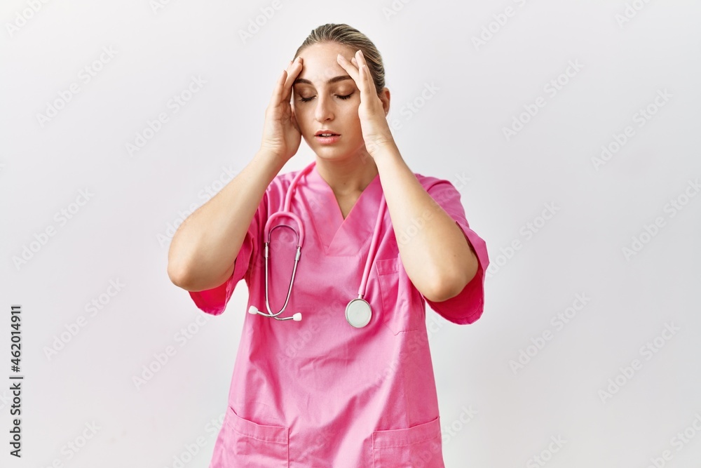 Young blonde woman wearing pink nurse uniform over isolated background suffering from headache desperate and stressed because pain and migraine. hands on head. Young blonde woman wearing pink nurse uniform over isolated background suffering from headache desperate and stressed because pain and migraine. hands on head.