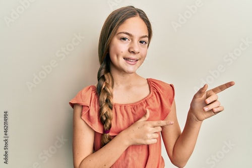 Beautiful brunette little girl wearing summer shirt smiling and looking at the camera pointing with two hands and fingers to the side.