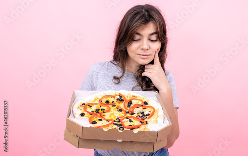 Attractive girl with pizza in a box for delivery on a pink background.