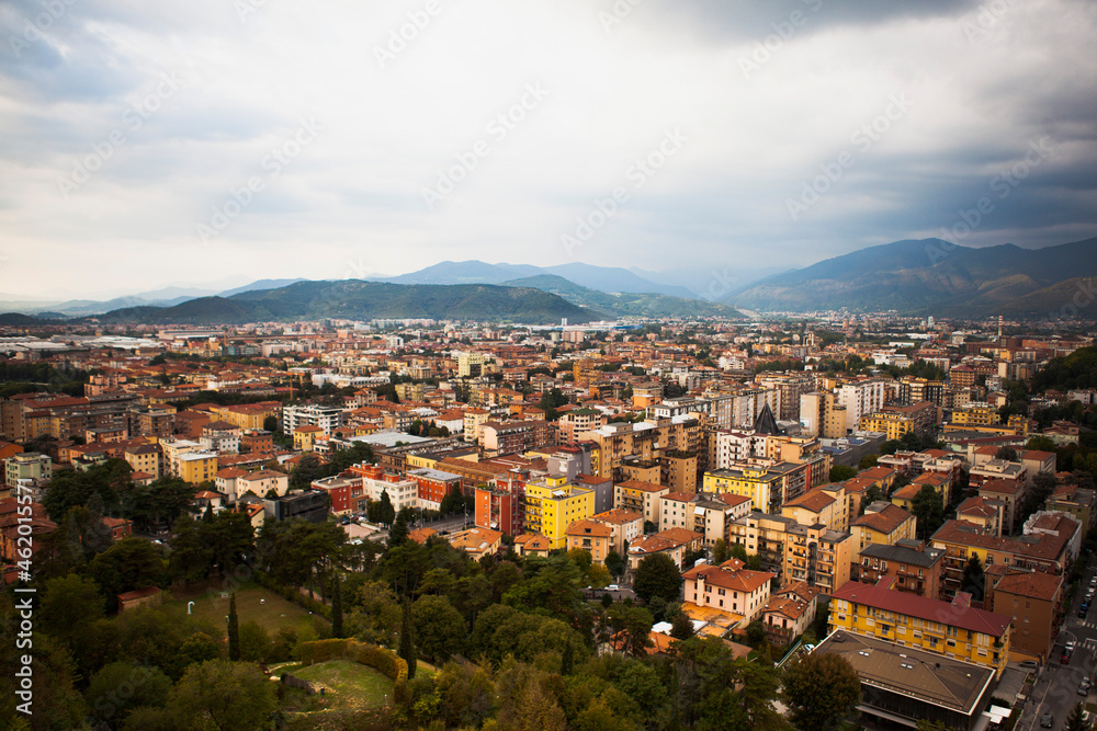 Aerial view of the mountains and  the modern centre of Brescia (Lombardy, Italy) with tiled red roofs, chimneys, cathedral's domes and tall white brick old towers. Traditional European architecture.