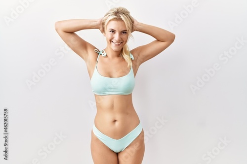Young caucasian woman wearing bikini over isolated background relaxing and stretching, arms and hands behind head and neck smiling happy