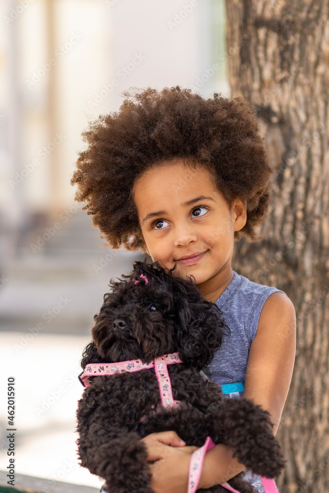 beautiful black afro American girl child hugging and playing with poodle dog