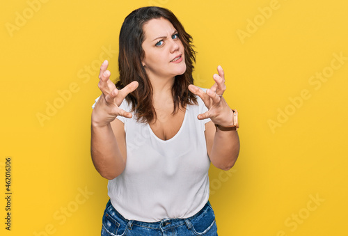 Young plus size woman wearing casual white t shirt shouting frustrated with rage, hands trying to strangle, yelling mad