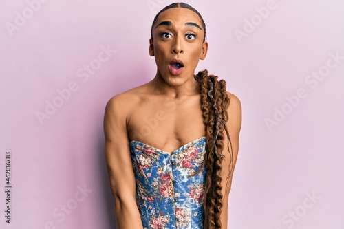 Hispanic man wearing make up and long hair wearing elegant corset afraid and shocked with surprise expression, fear and excited face.