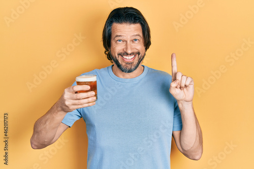 Middle age caucasian man drinking a pint of beer smiling with an idea or question pointing finger with happy face, number one